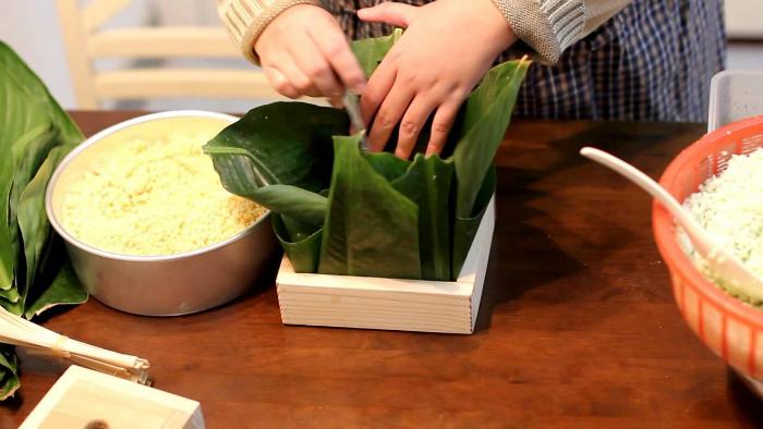 Dùng một chiếc khuôn và đặt lá chuối lên để gói bánh được vuông vức